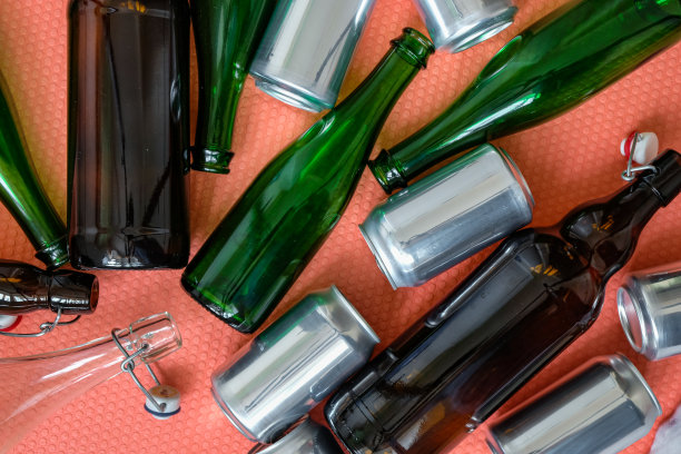 粉色背景上的玻璃瓶和铝罐。饮料容器。图片下载