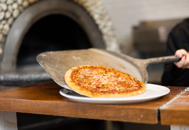 在披萨店的厨房里，穿着黑色制服的女厨师正在准备披萨，并把它从烤箱里拿出来图片下载