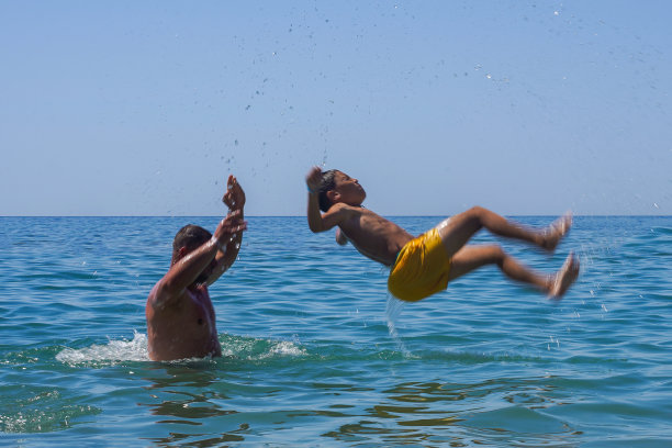 父亲把儿子扔进海里。海洋娱乐。全家暑假。模糊的照片在运动和溅起图片下载