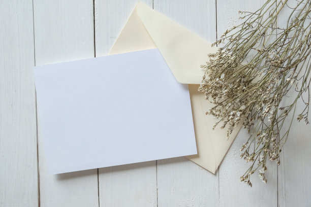 白色空白问候或邀请卡和信封与干花装饰在白色木制背景。模拟演示。图片下载