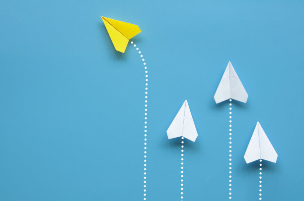 俯视图黄色纸飞机折纸飞向不同的方向留下其他白色飞机在蓝色背景。领导的概念图片下载