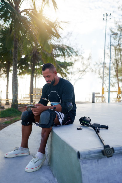 巴西中年成年滑板运动员，腿上有残疾，坐在公园里用手机发短信图片下载
