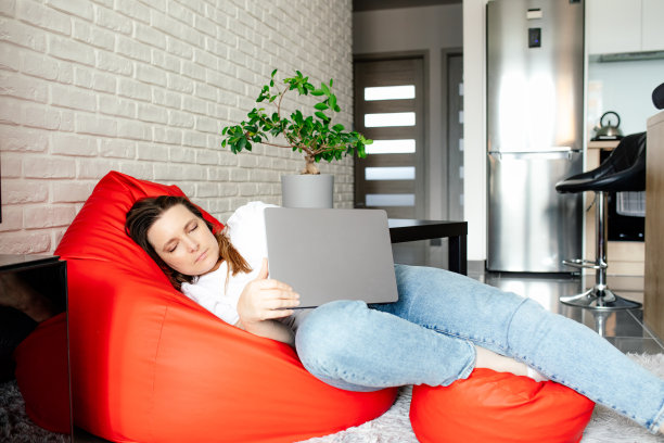 舒适和工作。自由职业者女人舒服地坐在包椅上，伸伸腿，用笔记本电脑工作。图片下载