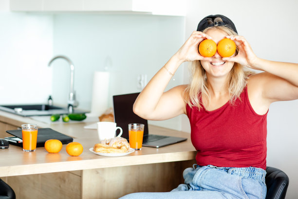 幽默。年轻的金发女郎在家里的厨房里享受着早餐的乐趣，有橙汁和新鲜的糕点。图片下载