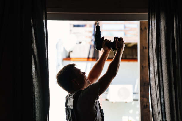 修理工的剪影正在修理阳台上的窗框或玻璃门。图片下载