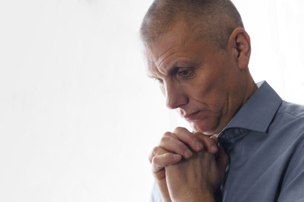 一个站在窗前的男人的肖像，他紧握双手在他面前，集中注意力，祈祷或思考图片下载