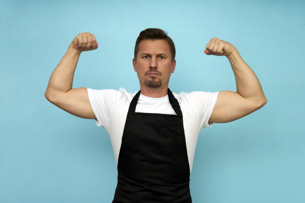 年轻的咖啡师穿着黑色围裙和蓝色背景的白色t恤图片下载