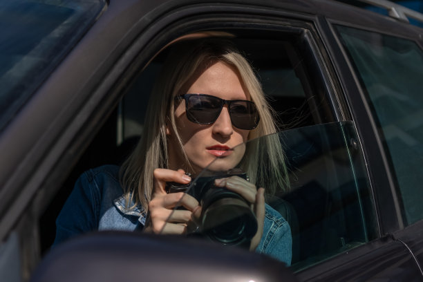 狗仔队的女人或女孩坐在她的车里拍名人的照片。车里有摄像头的间谍。私家侦探或狗仔队记者坐在车里，用相机拍照。图片下载