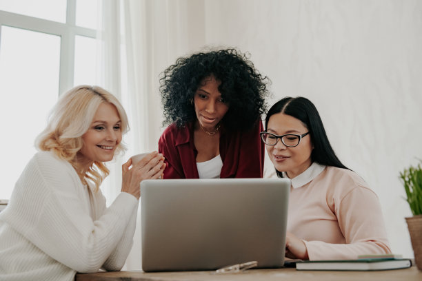 三个快乐的成熟女人一起坐在办公桌前使用笔记本电脑图片下载