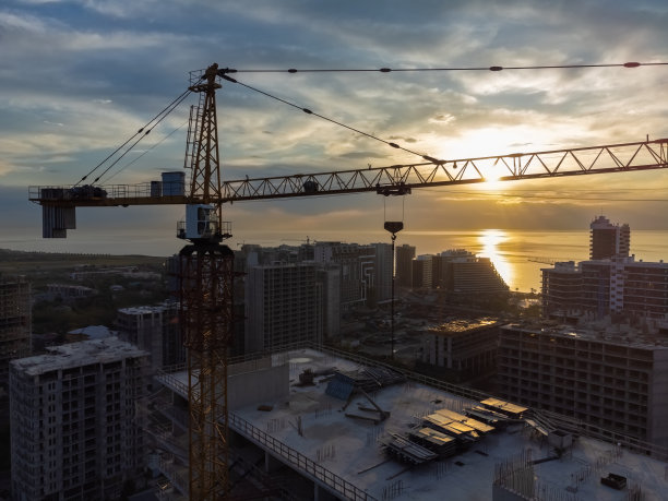 日落时建筑起重机的特写。在美丽日落的背景下，从无人机上看到的海滨多层建筑。建设理念图片下载