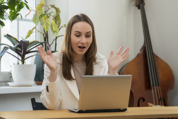 一位兴奋的欧洲女性坐在客厅的桌子旁，在使用笔记本电脑时表现出兴趣或惊讶图片下载