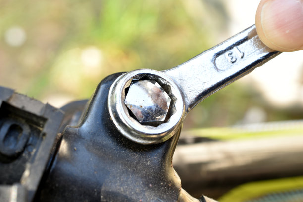 用环形扳手拧紧自行车车把螺栓的人的手。图片下载