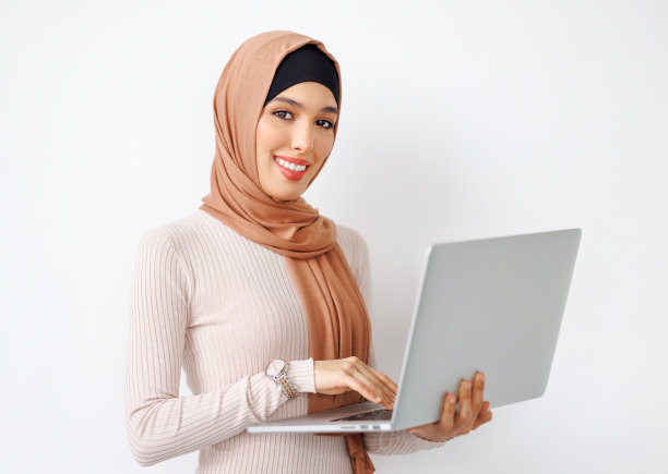 在灰色背景上手持笔记本电脑的微笑穆斯林美丽女性图片下载