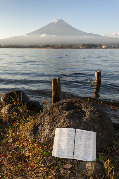 《圣经》(《诗篇》第121、122、123和124篇)倚靠在川口湖岸边的岩石上，背景是雄伟的富士山图片下载