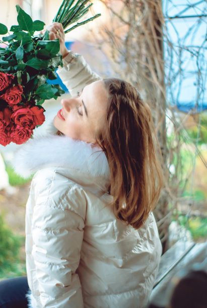 一个美丽的女人坐在长凳上享受玫瑰的香味。图片下载