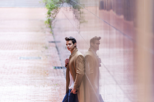 一个穿着大衣站在户外靠在墙上的时髦英俊的年轻人的肖像。图片下载