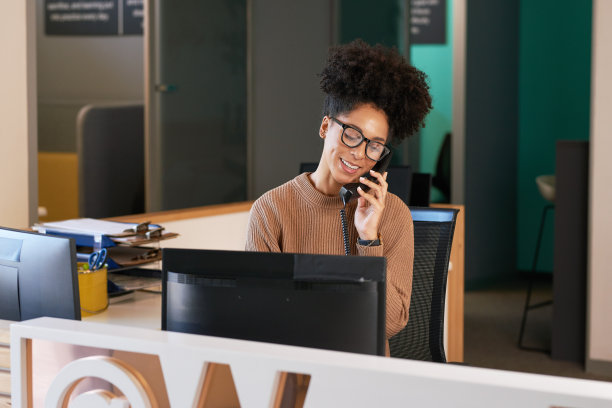 前台接待员在电话里微笑着，她是卷发的多民族妇女图片下载
