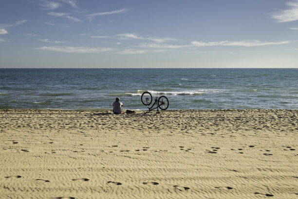 一个人骑着自行车看着大海休息。在天空或沙地上复制空间图片下载