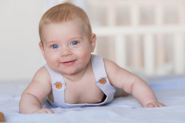 一个可爱的男孩在明亮的卧室里。一个新生的婴儿躺在床上。一个4个月大的孩子看着镜头，微笑着。儿童床上用品。家庭、怀孕和分娩。图片下载