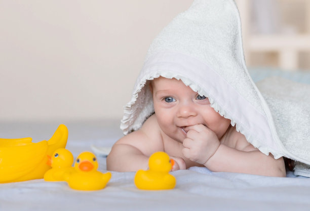 一个可爱的新生婴儿在洗完澡后躺在橡皮鸭的床上。一个头上裹着毛巾的4个月大的孩子看着镜头笑了。婴儿洗澡和卫生。图片下载