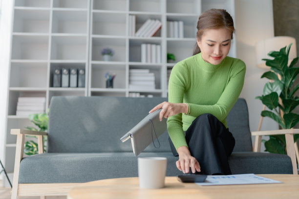美丽的亚洲女性用计算器计算家庭财务，发票和文书在桌子上，客厅室内。女性经济核算，现金流费用。图片下载