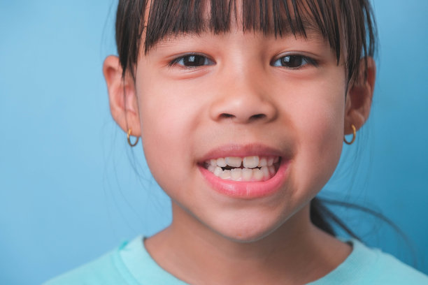 一个微笑的年轻女孩的特写，在蓝色的背景上露出她美丽的白牙齿。儿童健康的概念。图片下载
