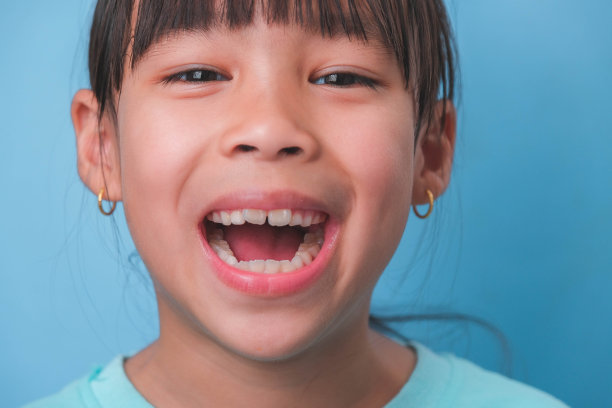 一个微笑的年轻女孩的特写，在蓝色的背景上露出她美丽的白牙齿。儿童健康的概念。图片下载