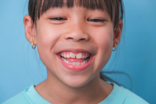 一个微笑的年轻女孩的特写，在蓝色的背景上露出她美丽的白牙齿。儿童健康的概念。图片下载