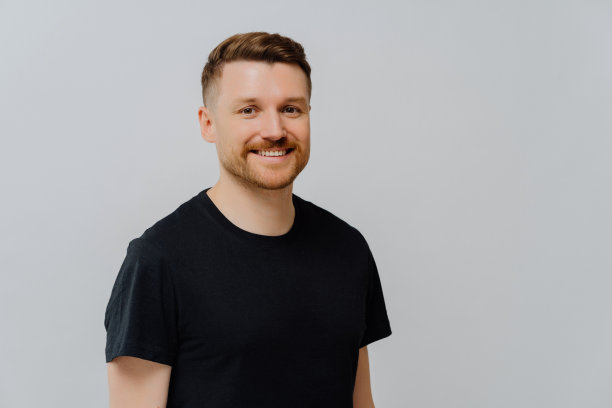 迷人的欧洲男人的肖像微笑着，无忧无虑，心情很好，穿着休闲的黑色t恤，在蓝色背景下为你的广告内容摆姿势。图片下载