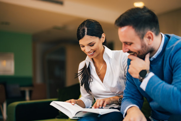 两个成年同事在办公室休息时微笑着看书。图片下载