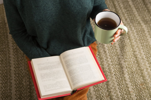 一个年轻的女人正坐在地毯上看书，端着一杯茶图片下载