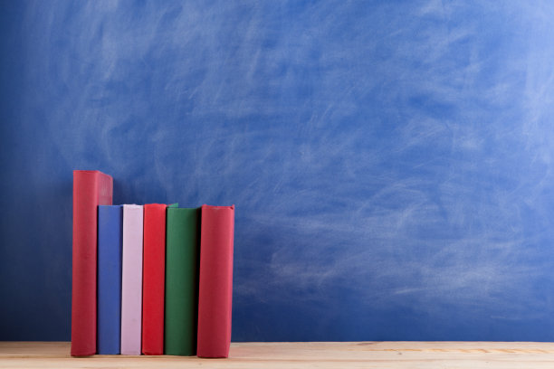 教育与阅读理念——木桌上的成组书籍，蓝色黑板背景。老师的桌子上图片下载