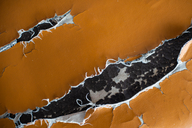 旧合成革棕色沙发被撕坏。沙发合成革内饰上旧裂损坏的皮革。图片下载