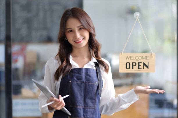 一位年轻的女企业家在咖啡店前挂着欢迎标语的肖像。漂亮的女服务员或女主人拿着平板电脑准备在餐馆里建议点菜。图片下载