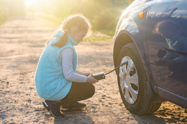 日落时分，一个小女孩在一条土路上用压缩机给汽车车轮打气图片下载