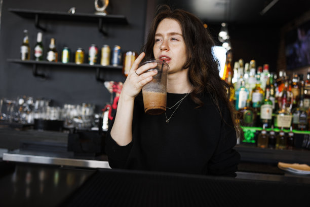 欢乐时光的夜总会醉酒派对:醉酒的年轻女子在吧台旁用吸管喝鸡尾酒。低角度视图图片下载