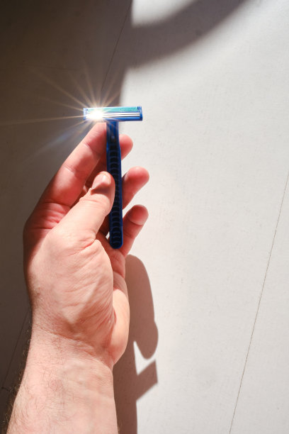 一个男人手里拿着刀片的一次性剃刀，背景很淡。男性面部护理概念图片下载