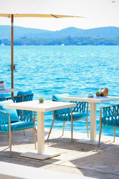 海滩俱乐部概念。一个时尚的美食角落或海滨咖啡馆的内部。餐厅餐桌，稻草天然椅子，白色木桌，makrome针织椅背，海景为背景图片下载