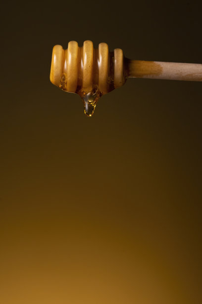 蜂蜜滴从木桶蜂蜜棒微距拍摄暗黄色背景图片下载