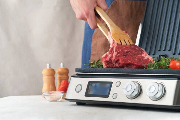 电烤架上的生牛排。厨师男手拿牛排肋眼与迷迭香，樱桃番茄和胡椒在现代电烤架。现代厨房的烹饪过程。俯视图，复制空间。图片下载