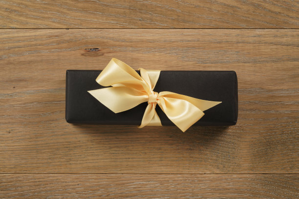 黑色矩形礼盒香槟色缎带蝴蝶结在橡木桌从上面图片下载