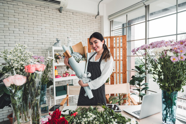 在花店里，一位年轻的花商手持一束自己精心准备的花束，准备送给顾客。图片下载