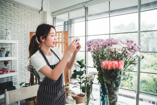 在花店里，年轻的花商正在为插在花瓶里的漂亮花朵拍照。图片下载