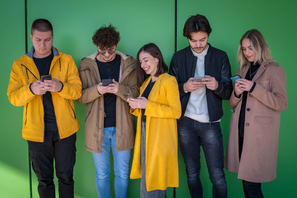 年轻人在户外使用智能手机——千禧一代享受社交媒体应用的新趋势——年轻人沉迷于科技——绿色背景图片下载