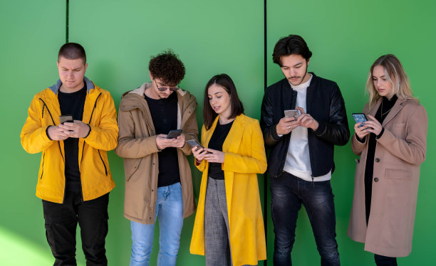 年轻人在户外使用智能手机——千禧一代享受社交媒体应用的新趋势——年轻人沉迷于科技——绿色背景图片下载