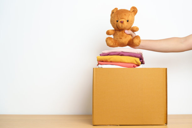 儿童捐赠，慈善，志愿者，给予和交付的理念。亲手捐赠小熊娃娃和衣服到家里的纸板箱，以支持和帮助穷人，难民和无家可归的人。文本复制空间图片下载