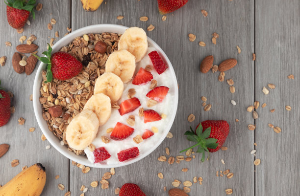 格兰诺拉麦片配草莓、坚果、牛奶和香蕉放在桌子上的碗里。健康的谷类早餐。图片下载