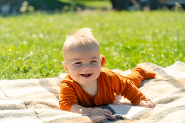 快乐的宝宝躺在阳光明媚的草地上的毯子上。儿童户外。图片下载