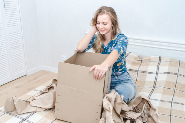 微笑的年轻女子在家里的床上打开纸箱。交付包裹。互联网秩序图片下载