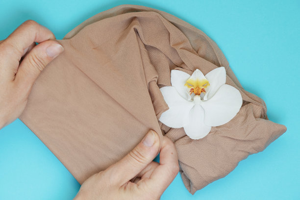 女人的手伸展尼龙裤袜和白色兰花花在彩色背景图片下载